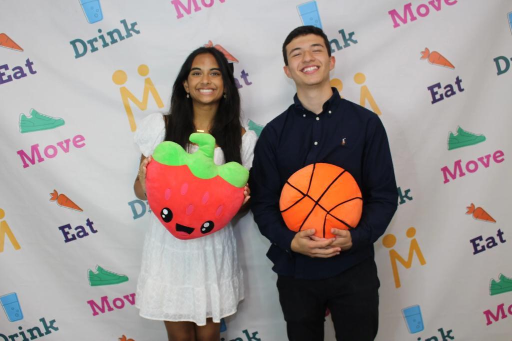 Álvaro Saldarriaga Arcila holding a stuffed basketball and Pratima Yellayi holding a stuffed strawberry and standing in front of a colorful backdrop.