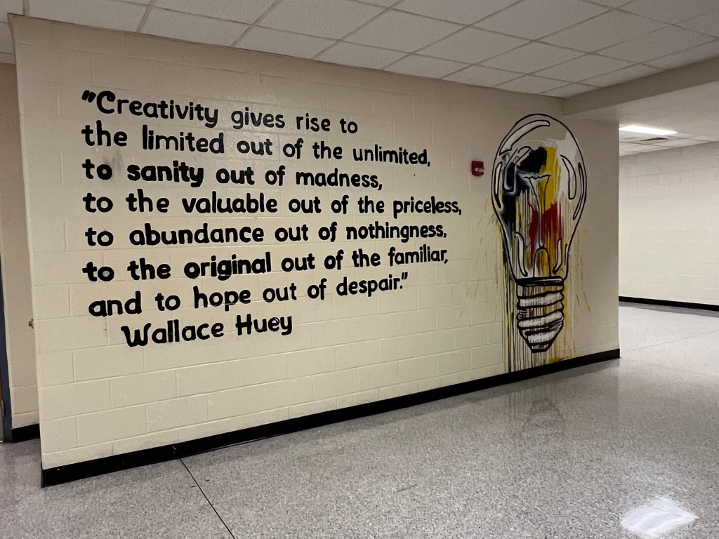 A mural painted on a cinder block wall. A painting of a lightbulb is next to a quote by Wallace Huey that reads, creativity gives rise to the limited out of the unlimited, to sanity out of madness, to the valuable out of the priceless, to abundance out of nothingness, to the original out of the familiar, and to hope out of despair.